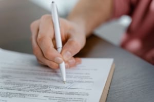 A person signing real estate documents, representing the buying or selling of residential properties in Portland.
