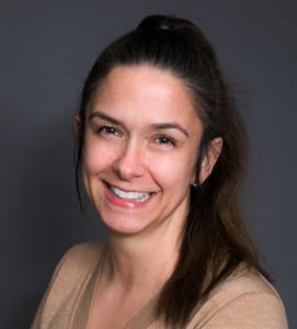 Professional headshot of smiling real estate agent against neutral gray background
