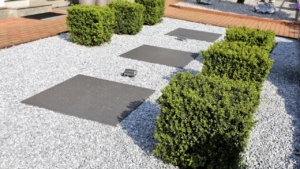 Gravel garden with square stepping stones, trimmed boxwood shrubs, and modern landscape lighting