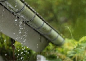 Leaking gutter dripping rainwater along roof edge with greenery in background