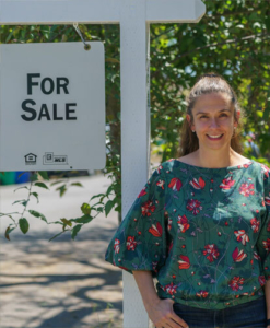Real estate agent standing beside for sale sign in Portland neighborhood