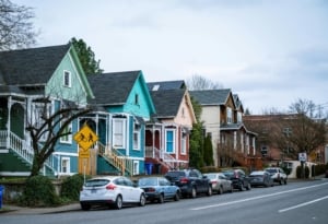 Charming row of colorful historic-style homes in a walkable neighborhood with on-street parking, mature trees, and bike/pedestrian-friendly signage