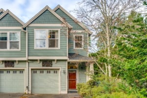 Charming Portland duplex with beautiful green siding, garage, and trees, perfect for modern urban living.