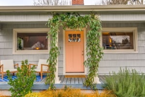 Charming entryway of a single-family home featuring a pastel door, cozy seating, and lush greenery, ideal for Portland living.