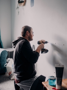 Man drills anchors into wall to secure furniture safely in his home.