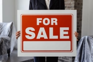 Real estate agent holding a 'For Sale' sign in a modern home, showcasing Portland real estate investment opportunities.