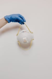 A hand in a blue glove holds an N95 mask, emphasizing safety for homeowners and real estate agents during property tours.